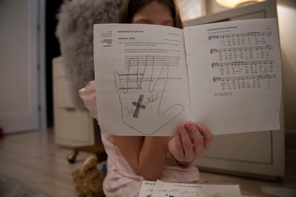 Mary Joyce’s daughter holds up a drawing she did over a booklet depicting parental vows of a Baptism the booklet is one of the items kept in her “memory drawer” at the family’s home in Nashville, Tenn., Tuesday, Dec. 5, 2023.