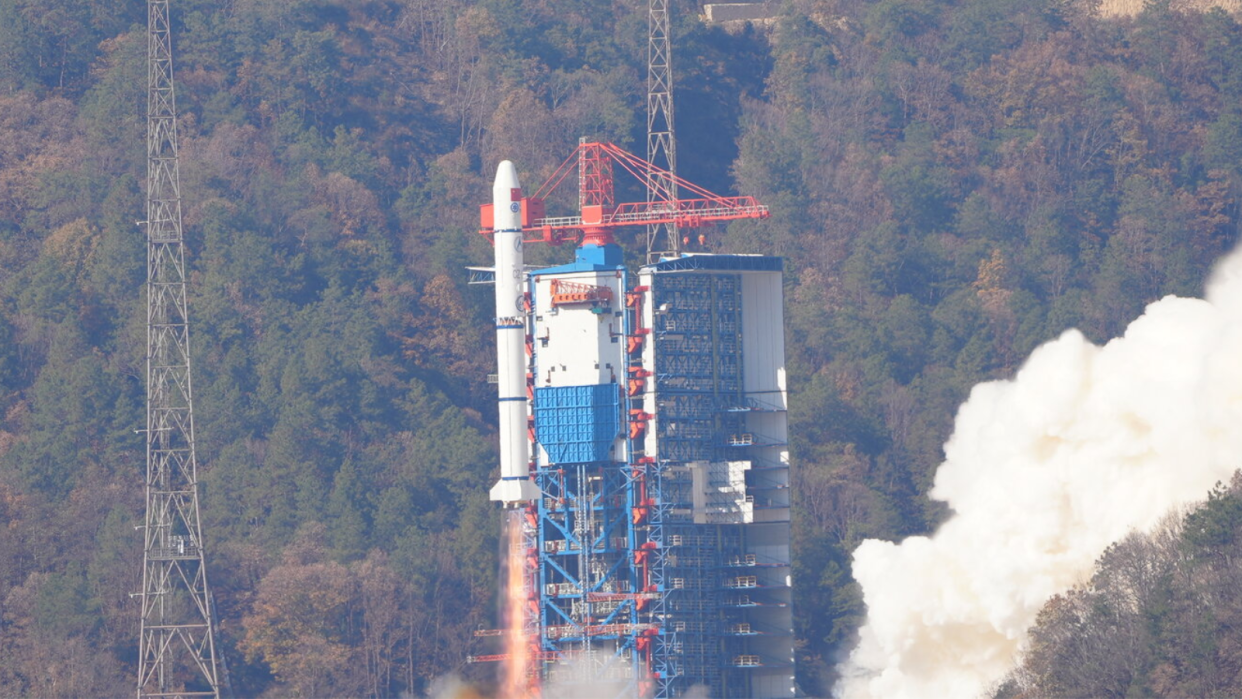  A white rocket launches with a tree-covered hill in the background. 