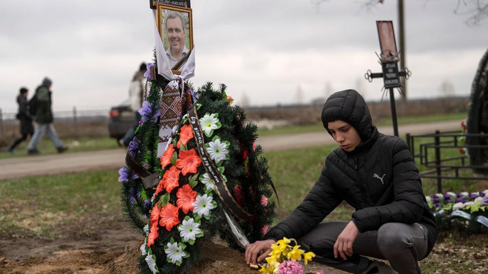 Yura Nechyporenko, 15, places a chocolate at the grave of his father Ruslan Nechyporenko at the cemetery in Bucha, on the outskirts of Kyiv, Ukraine, on Thursday, April 21, 2022. The teen survived an attempted killing by Russian soldiers while his father was killed, and now his family seeks justice.