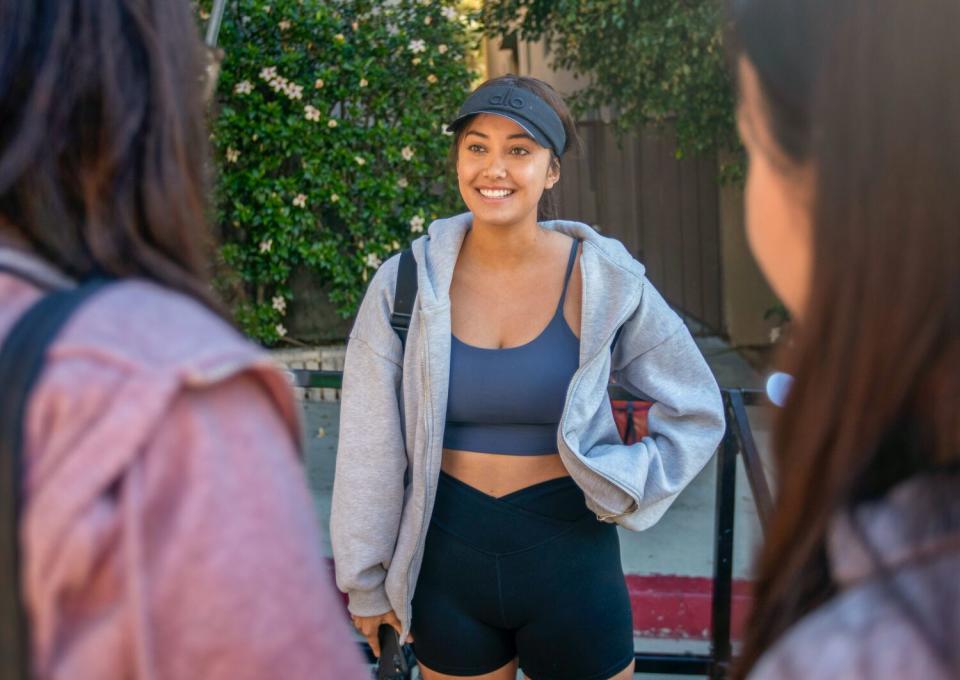 Monica Figueroa, middle, greeting two people facing her on either side of the frame. All are dressed in workout clothes.