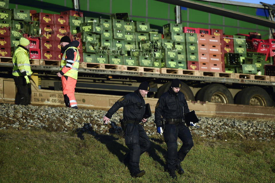 Police walk by a freight train after a train accident on the Great Belt Bridge in Nyborg, Denmark, Wednesday, Jan. 2, 2019. A Danish passenger train apparently hit falling cargo from a passing freight train Wednesday, an accident that killed at least six people and injured over a dozen others as it crossed a bridge linking the country's islands, authorities said. Authorities said the trains were going past each other in opposite directions. Aerial TV footage showed one side of front of the passenger train had been ripped open. (Mads Claus Rasmussen/Ritzau Scanpix via AP)