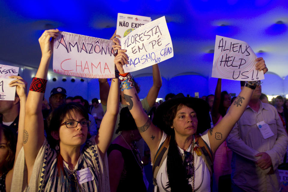 Demonstrators hold signs that read in Portuguese "Standing Forest, Fascism" and "Amazons calls" during a protest at the Latin America and Caribbean Climate Week workshop in Salvador, Bahia state, Brazil, Wednesday, Aug. 21, 2019. Brazil is hosting a week-long UN workshop on climate change in the northern state of Bahia, which the environment minister tried to cancel earlier this year. (AP Photo/Arisson Marinho)