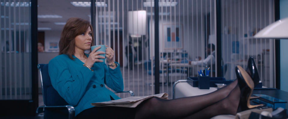 Robbie (Elizabeth Banks) sits in an office leaning back in a chair, with her feet up on the desk, drinking from a mug