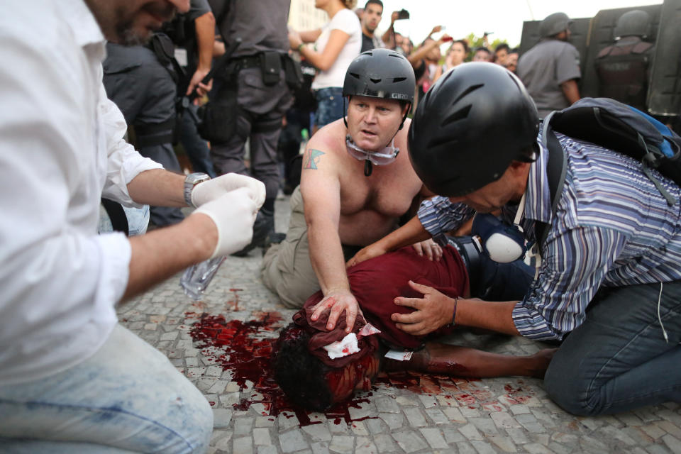 Cameraman Andrade Santiago is helped after he was injured during violent clashes with police during a protest against a bus fare increase in Rio de Janeiro, Thursday, Feb. 6, 2014. Police said Thursday that the cameraman for the Band TV station was injured in the protest and is in serious condition. It was not clear if the journalist was hit by a homemade explosive thrown by protesters or a stun grenade shot by police. (AP Photo/Leo Correa)