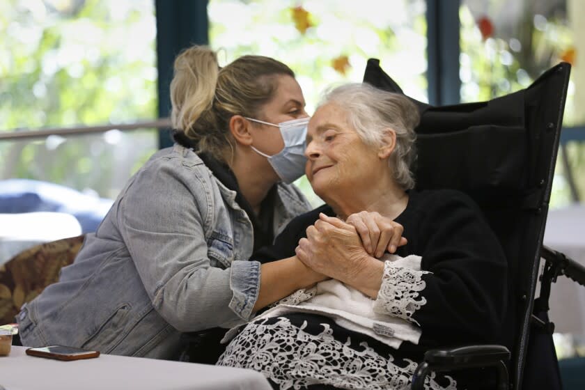 Mission Hills, Los Angeles, California-Nov. 25, 2021-At the Arafat Nursing Facility, Ruzanna Grigoryan, left, of Chatsworth, California, visits with her grandmother Anahit Papiryan, age 82, originally from Yevan, Armenia, during festivities on Thanksgiving Day. Many of Anahit's family members visit her on a daily basis. The Ararat Facility, which primarily serves the Armenian community, held a special Thanksgiving celebration for the residents on Thursday, Nov. 25, 2021. (Carolyn Cole / Los Angeles Times)