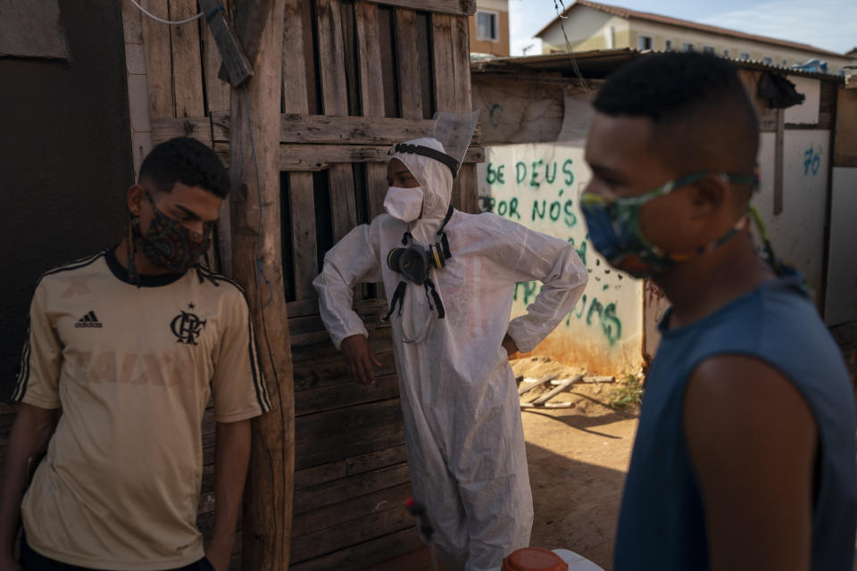 Volunteer Welington Goncalves, center, takes a break from sanitization duties to help contain the spread of the new coronavirus in an area occupied by squatters in a poor region of Rio de Janeiro, Brazil, Friday, June 26, 2020. For the 21-year-old volunteer, who lives in this occupation, the sanitization is a way to avoid the COVID-19 and if it was not for him and other volunteers working on it, "the situation would be worse". (AP Photo/Leo Correa)