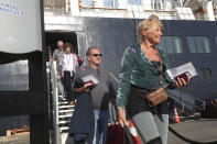 Passenger disembark from the MS Westerdam, back, at the port of Sihanoukville, Cambodia, Saturday, Feb. 15, 2020. After being stranded at sea for two weeks because five ports refused to allow their cruise ship to dock, the passengers of the MS Westerdam were anything but sure their ordeal was finally over. (AP Photo/Heng Sinith)