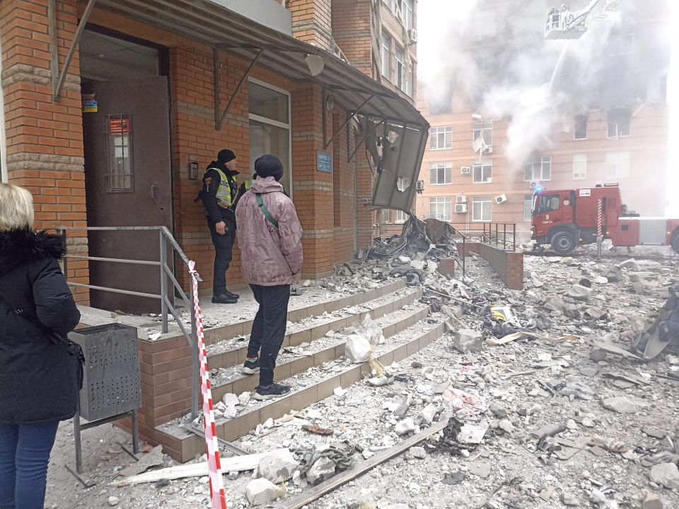 People and a Ukrainian serviceman watch as firefighters work to extinguish a fire at a damaged apartment building after a Russian attack in Odesa, Ukraine, Friday, Dec. 29, 2023. (AP Photo/Artem Perfilov)