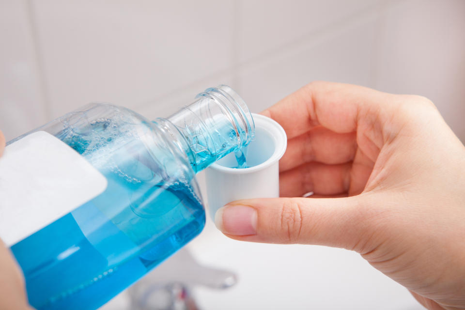 Pouring mouthwash into a cap over a bathroom sink