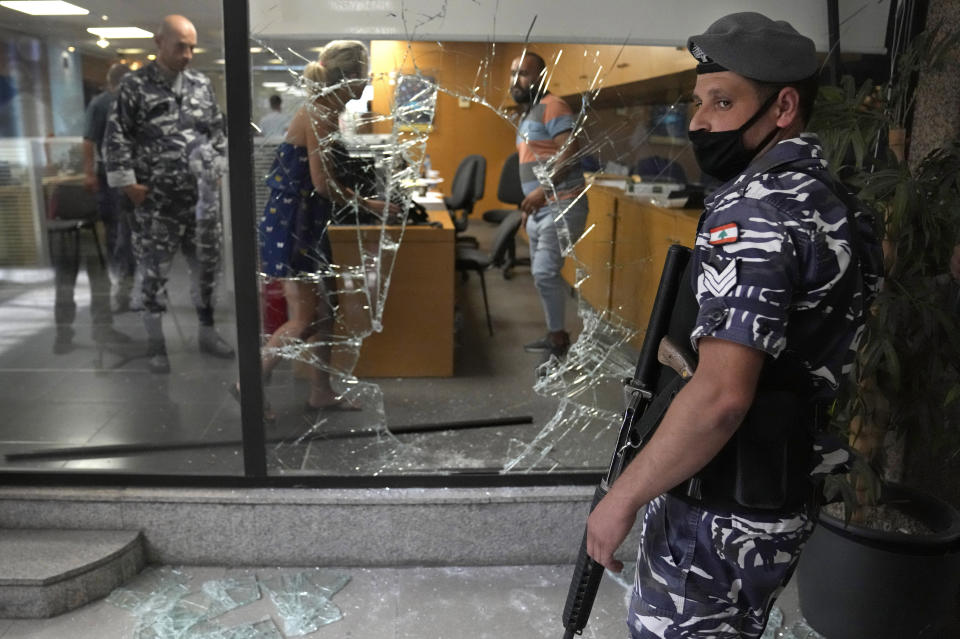 A Lebanese policeman stands guard next to a bank window that was broken by depositors to exit the bank after attacking it trying to get their money, in Beirut, Lebanon, Wednesday, Sept. 14, 2022. An armed woman and a dozen activists broke into a Beirut bank branch on Wednesday, taking over $13,000 from what she says were from their trapped savings. Lebanon's cash-strapped banks since 2019 have imposed strict limits on withdrawals of foreign currency, tying up the savings of millions of people. (AP Photo/Hussein Malla)