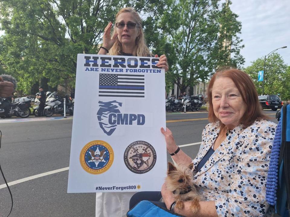Trish Gotchev holds a Heroes are Never Forgotten poster outside First Baptist Church before the processional for CMPD Officer Joshua Eyer. Seated is Kathy Doty Queen and service dog George. They came from Fort Mill.