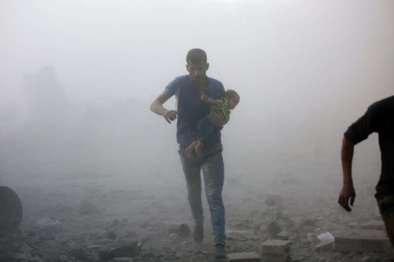 A Syrian man carrying a child emerges from a dust cloud following a reported airstrike on Kafr Batna, in the rebel-held Eastern Ghouta area, on the outskirts of the capital Damascus, on September 30, 2016