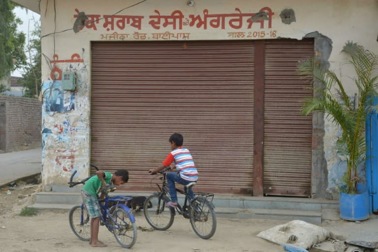 Children cycle in front of a closed liquor shop near a national highway on the outskirts of Amritsar in northern India