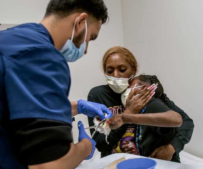 TORRANCE, CA - AUGUST 8, 2022: Staneisha Matthews holds tight to her daughter La'Veyah Mosley,12, as a physician's assistant carefully removes a bandage off La'Veyah's left hand on August 8, 2022 in Torrance, California. On July 5, La'Veyah was severely injured after she used a sparkler to light what she thought was a smoke bomb, but it turned out to be an illegal M80 firecracker., which a friend found in the street. La'Veyah suffered corneal abrasions in both eyes, ruptured eardrums and fractures in her forearms and fingers in her right hand. Her wrist bones were dislocated by the blast. Those would heal. But she lost all her fingers on her left hand, and her right hand was severely burned.(Gina Ferazzi / Los Angeles Times)