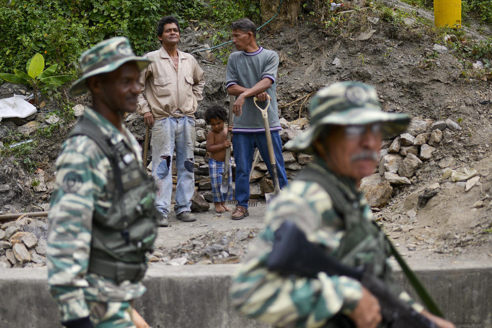 Workers look at soldiers taking part in an invasion drill in Caracas, Venezuela, Saturday, Feb. 15, 2020. Venezuela's President Nicolas Maduro ordered two days of nationwide military exercises, including the participation of civilian militias. (AP Photo/Matias Delacroix)