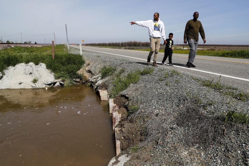 A small boy walks with two men on the side of a road near floodwaters.