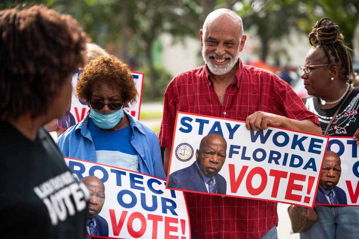 Rolando Chang Barrero of the Palm Beach County Democratic Hispanic Caucus smiles while holding a "Stay Woke" sign at Howard Park on June 22, 2023, in West Palm Beach, Florida. The "Stay Woke" Florida bus tour is part of a rolling statewide initiative to encourage voting, as well as protest against state efforts to end diversity and inclusion programs.