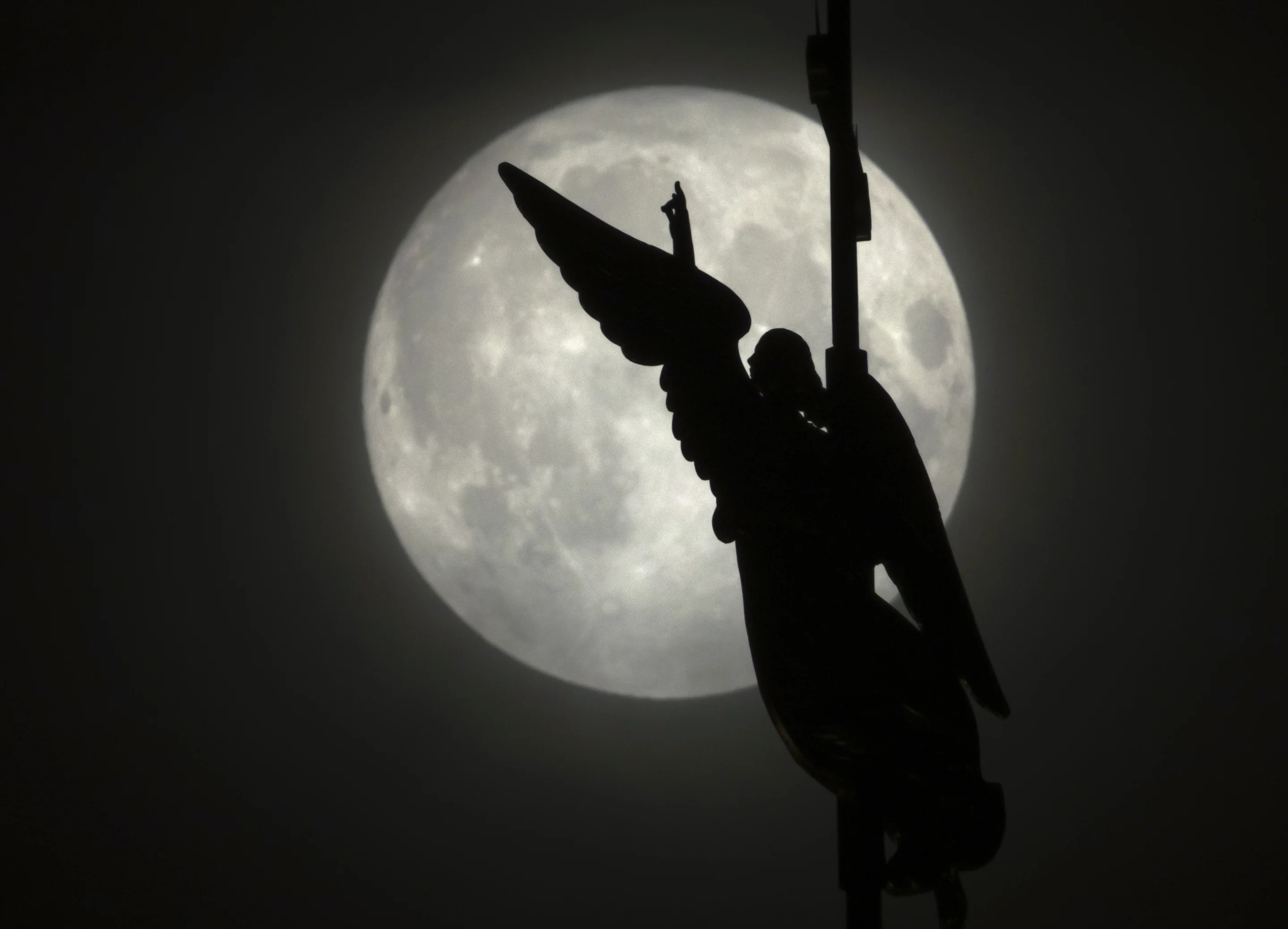 An angel weather vane atop a spire of the Saints Peter and Paul Cathedral, is silhouetted by the rising full moon, on Tuesday, in St. Petersburg, Russia.