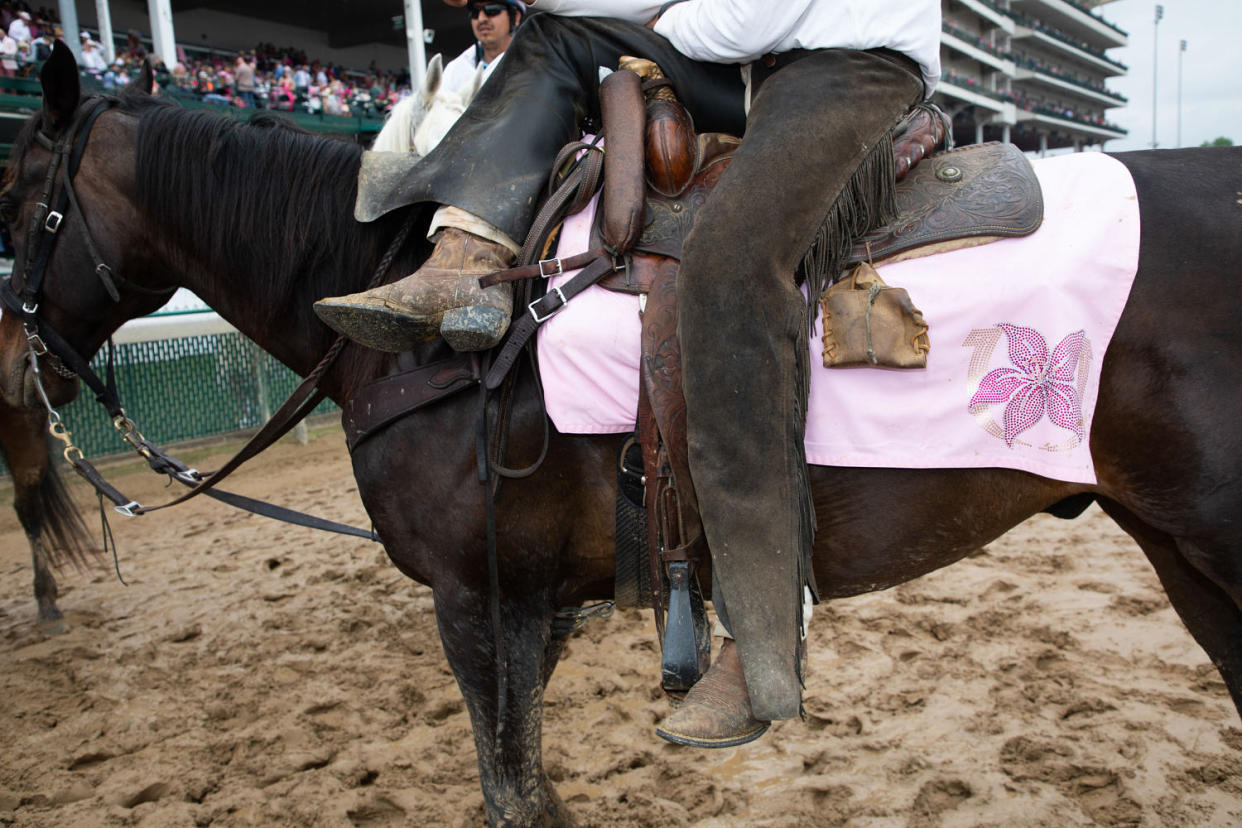 A man in muddy boots and chaps sits on top of a horse on a muddy track.