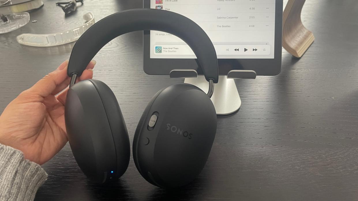  Sonos Ace wireless headphones being held in front of an iPad. 