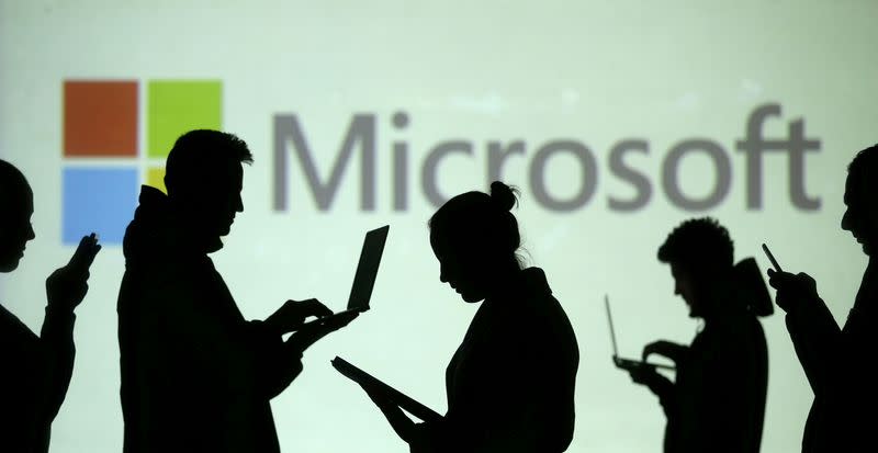 FILE PHOTO: Silhouettes of laptop and mobile device users are seen next to a screen projection of Microsoft logo