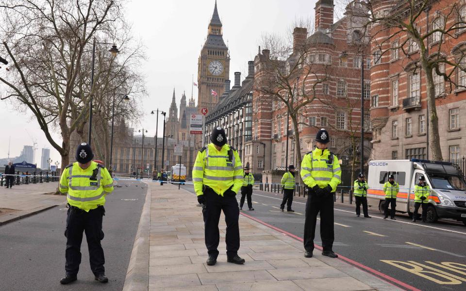 British police officers bow their heads as they stand near a police cordon directly ourside New Scotland Yard and within sight of the Houses of Parliament - AFP or licensors