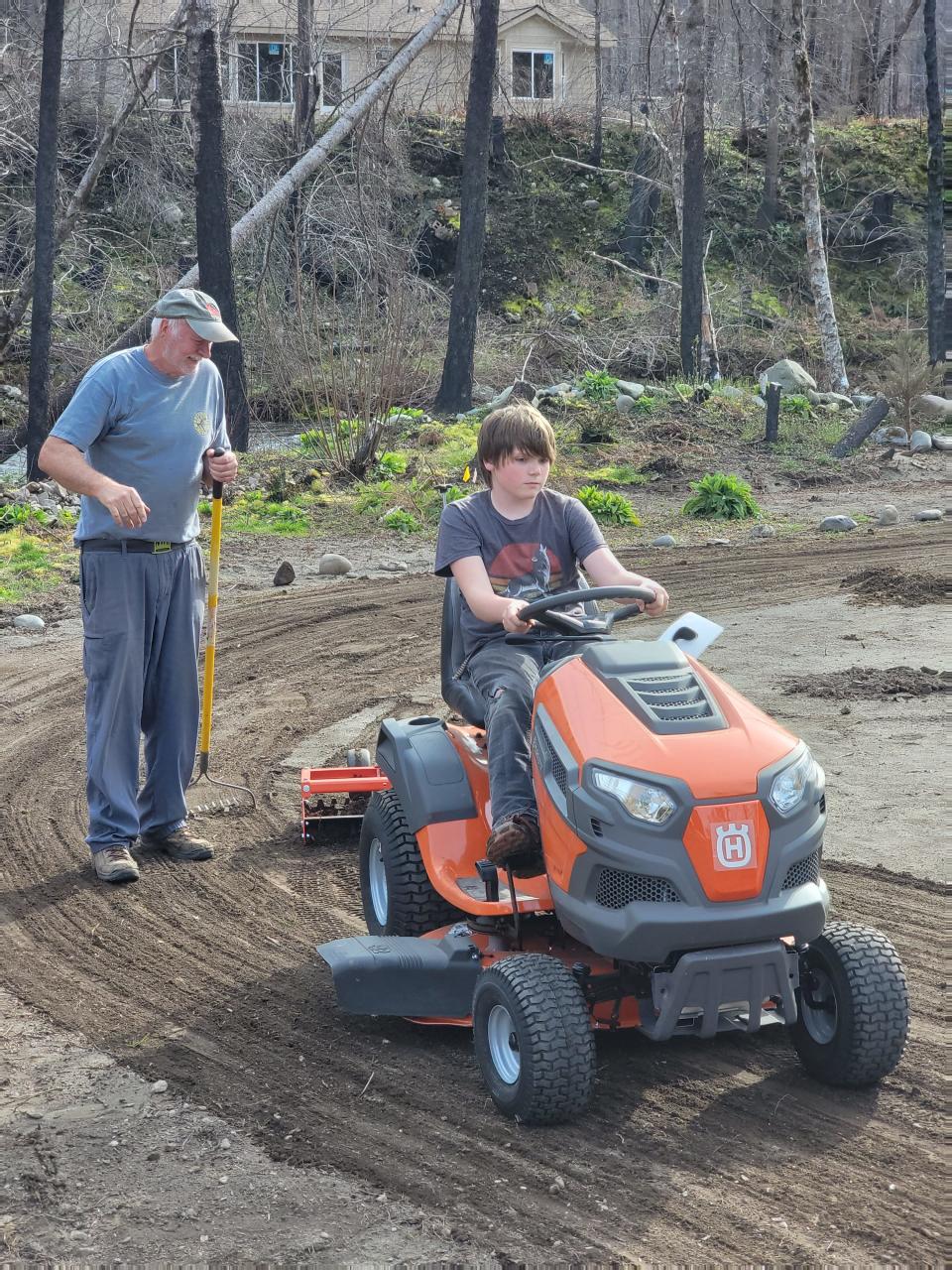 Elliott Baker, 13, drives a riding lawn mower on property of his family's cabin in Little North Santiam. The original cabin was burned during the Beachie Creek Fire in 2020. A large part of the rebuilding process has been planting and landscaping.