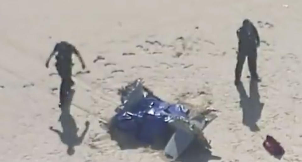 Two uniform police officers inspect washed up aircraft wreckage on North Stradbroke Island..