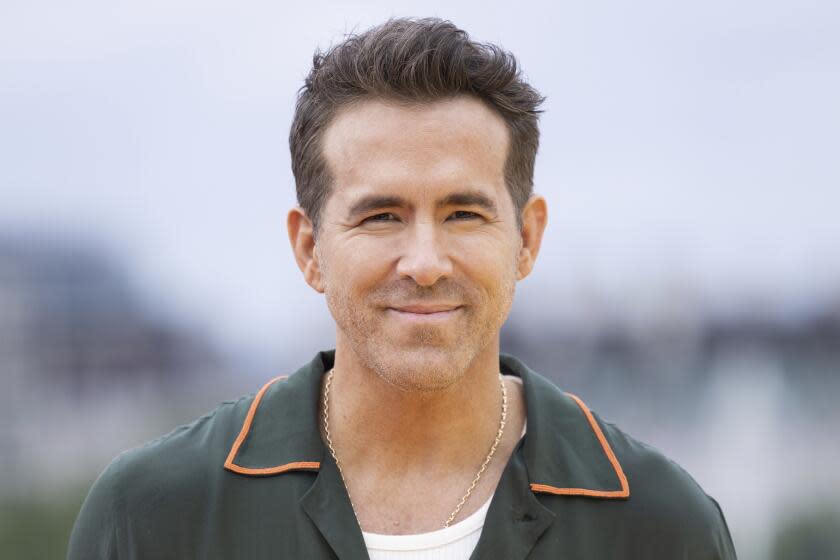 Ryan Reynold grinning wearing a green collard shirt.