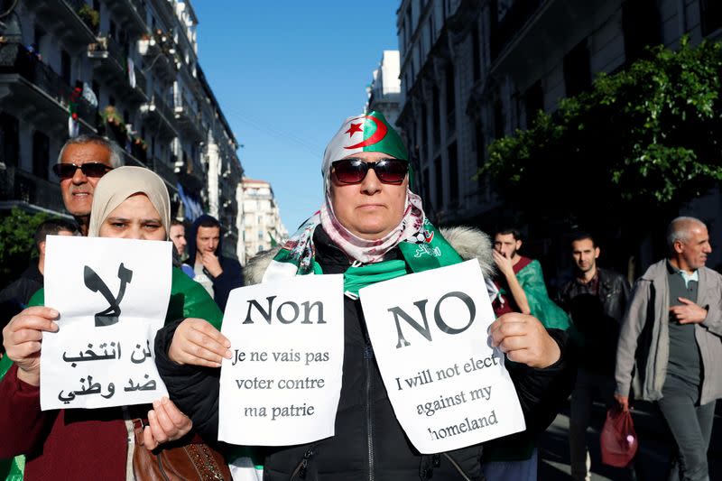 Demonstrators hold signs as they take part in a protest to demand for the presidential election scheduled for next week to be cancelled, in Algiers