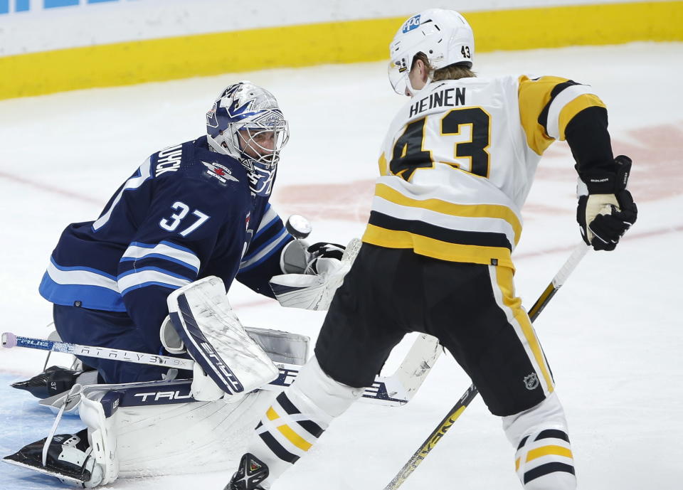 Winnipeg Jets goaltender Connor Hellebuyck (37) saves a shot by Pittsburgh Penguins' Danton Heinen (43) during second-period NHL hockey game action in Winnipeg, Manitoba, Saturday, Nov. 19, 2022. (John Woods/The Canadian Press via AP)