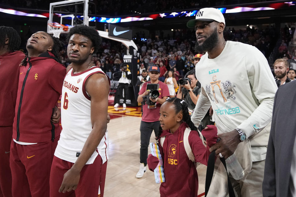 Southern California guard Bronny James (6) stands on the court with the rest of his team as his father, LeBron James, walks by prior to an NCAA college basketball game against Long Beach State Sunday, Dec. 10, 2023, in Los Angeles. (AP Photo/Mark J. Terrill)