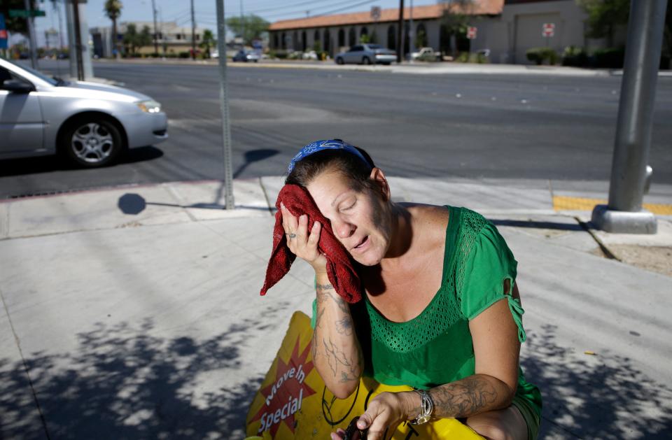 Amanda Ouellet wipes her face with a cold, wet towel to cool off while working outside holding an advertising sign in Las Vegas. A report from America's doctors says climate change is making us sick.