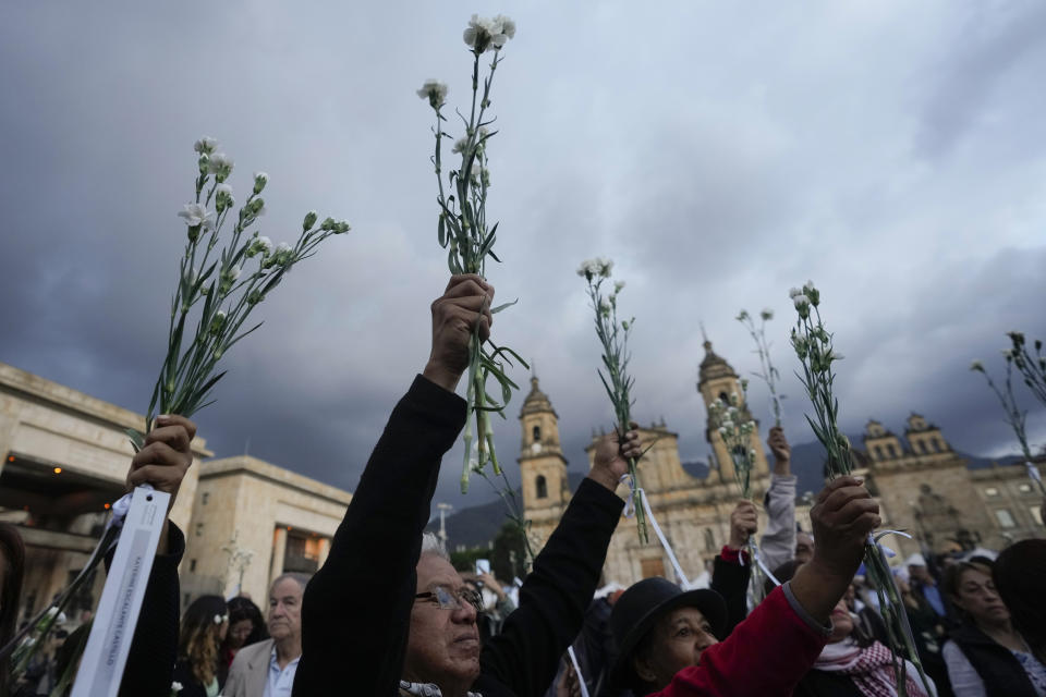 People hold flowers during an event to remember former guerrillas and social leaders who have been killed since the 2016 signing of a peace agreement between rebels of the Revolutionary Armed Forces of Colombia, FARC, and the government, in Bogota, Colombia, Tuesday, Feb. 20, 2024. (AP Photo/Fernando Vergara)