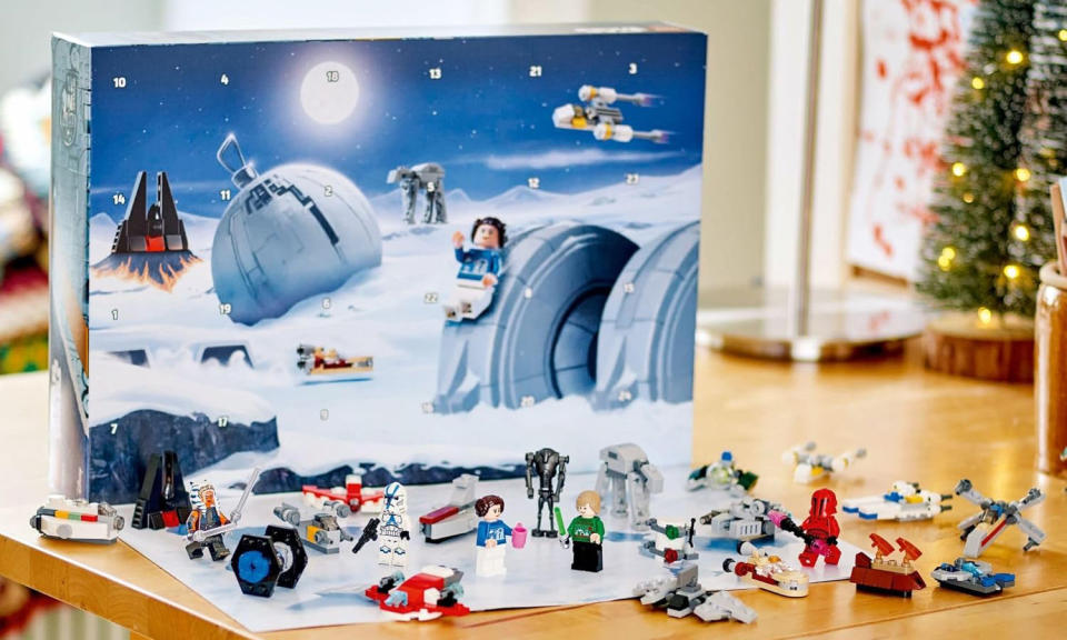 Un calendario de adviento de Lego Star Wars está dispuesto sobre una mesa con un árbol de Navidad al fondo. 