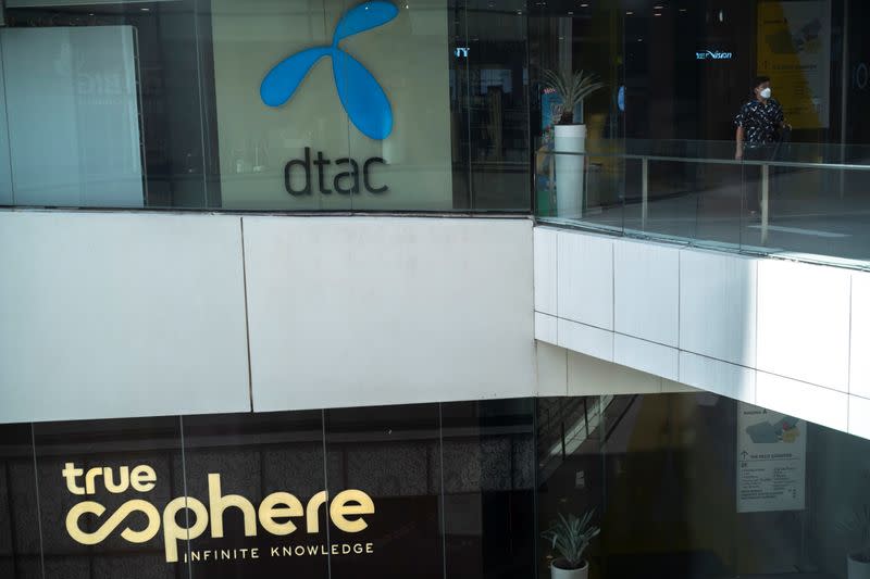 Man walks next to logo of the DTAC Public Company Limited and logo of True Corp. in Bangkok