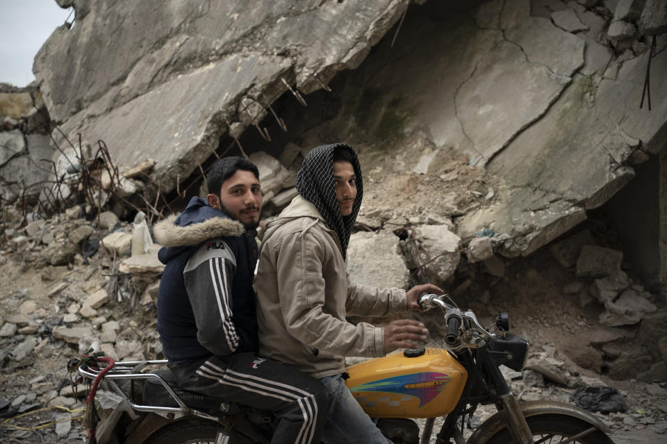 In this Thursday, March 12, 2020 photo, two Syrians pose for a photo as they ride a motorcycle in a neighborhood heavily damaged by airstrikes, in Idlib, Syria. Idlib city is the last urban area still under opposition control in Syria, located in a shrinking rebel enclave in the northwestern province of the same name. Syria’s civil war, which entered its 10th year Monday, March 15, 2020, has shrunk in geographical scope -- focusing on this corner of the country -- but the misery wreaked by the conflict has not diminished. (AP Photo/Felipe Dana)