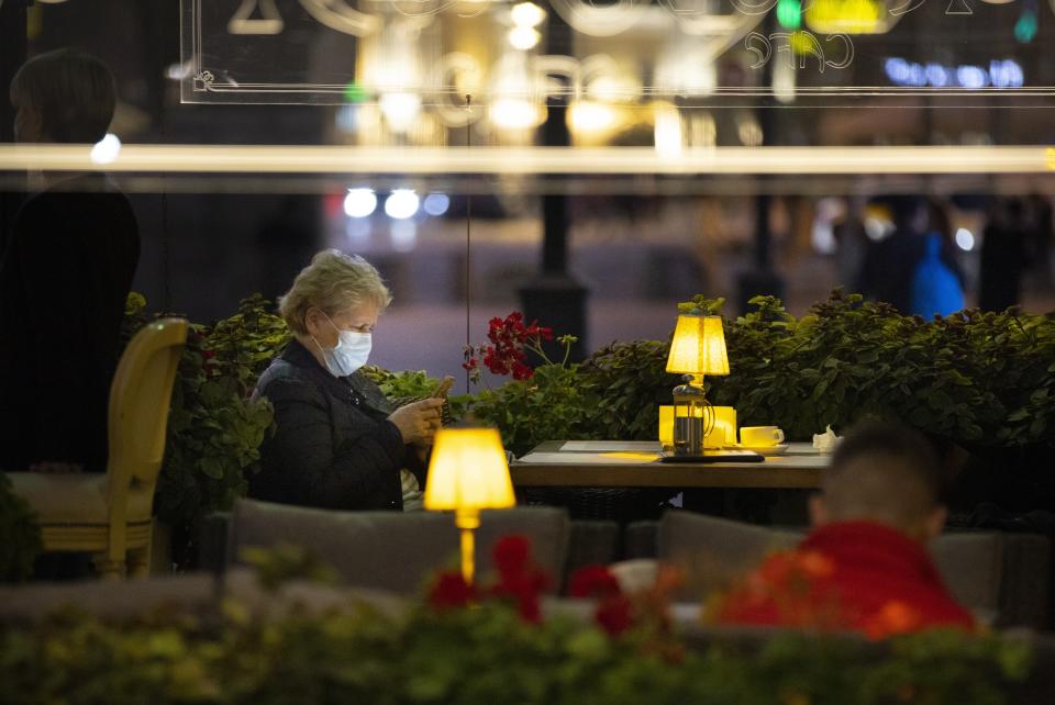 A woman, wearing a face mask to protect against coronavirus enjoys a warm evening sitting at a street-side cafe in the center of Moscow, Russia, Friday, Sept. 25, 2020. Moscow authorities have issued a recommendation for the elderly to stay at home and for employers to allow as many people as possible to work remotely, following a rapid growth of the coronavirus caseload in the Russian capital. (AP Photo/Alexander Zemlianichenko)