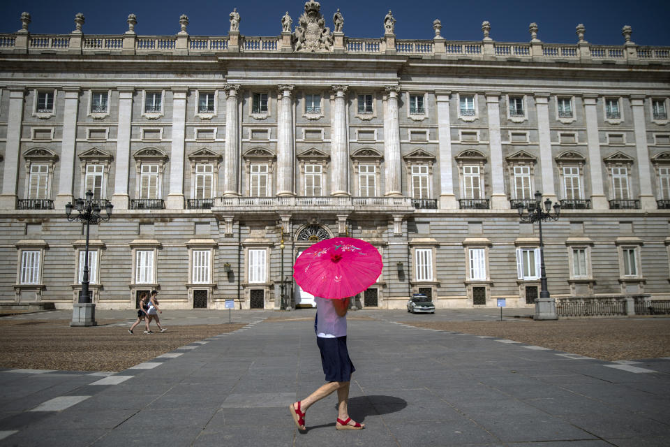 A woman with an umbrella walks past the Royal Palace during a heatwave in Madrid, Spain, Friday, Aug. 13, 2021. Stifling heat is gripping much of Spain and Southern Europe, and forecasters say worse is expected to come. (AP Photo/Andrea Comas)