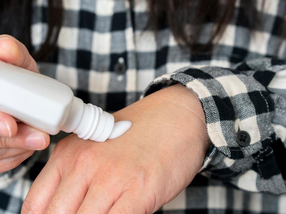 A person squeezes a bottle of cream on to the top of their hand.