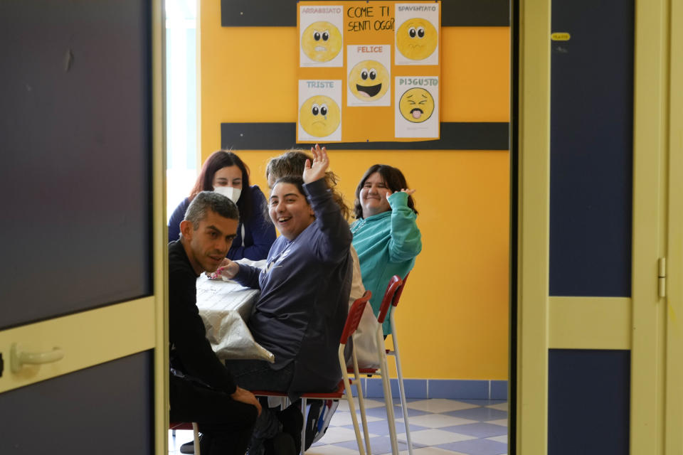 Marika Pucci, center, and Chiara Santarelli, right, waves to the photographer as they sit inside a facility of the Chicco community of L'Arche, an International charity that helps people with intellectual disabilities, in Ciampino, near Rome, Wednesday, March 22, 2023. The findings of expert reports commissioned by L’Arche itself reveal that their founder, Jean Vanier, perverted Catholic doctrine to justify his own sexual compulsions and abuse women and that the movement he created had at its core a secret, a mystical-sexual “sect” founded for the precise purpose of hiding the sect’s deviant activities from church authorities. (AP Photo/Gregorio Borgia)