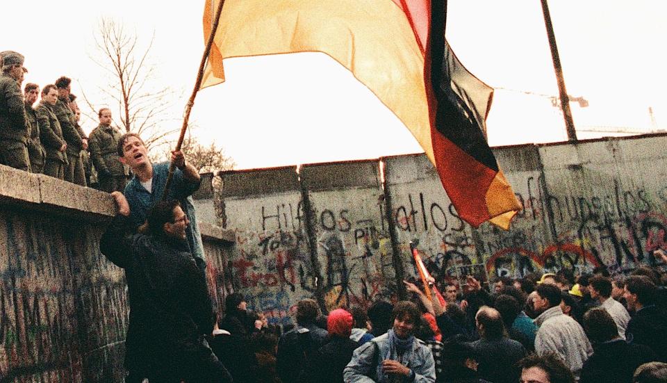 A man waves the German national flag under the gaze of East-German border guards on top of the Berlin Wall, Berlin, Germany, 10th November 1989.