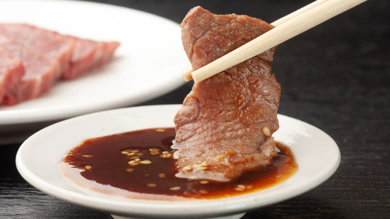 Chopsticks dipping meat in tare sauce