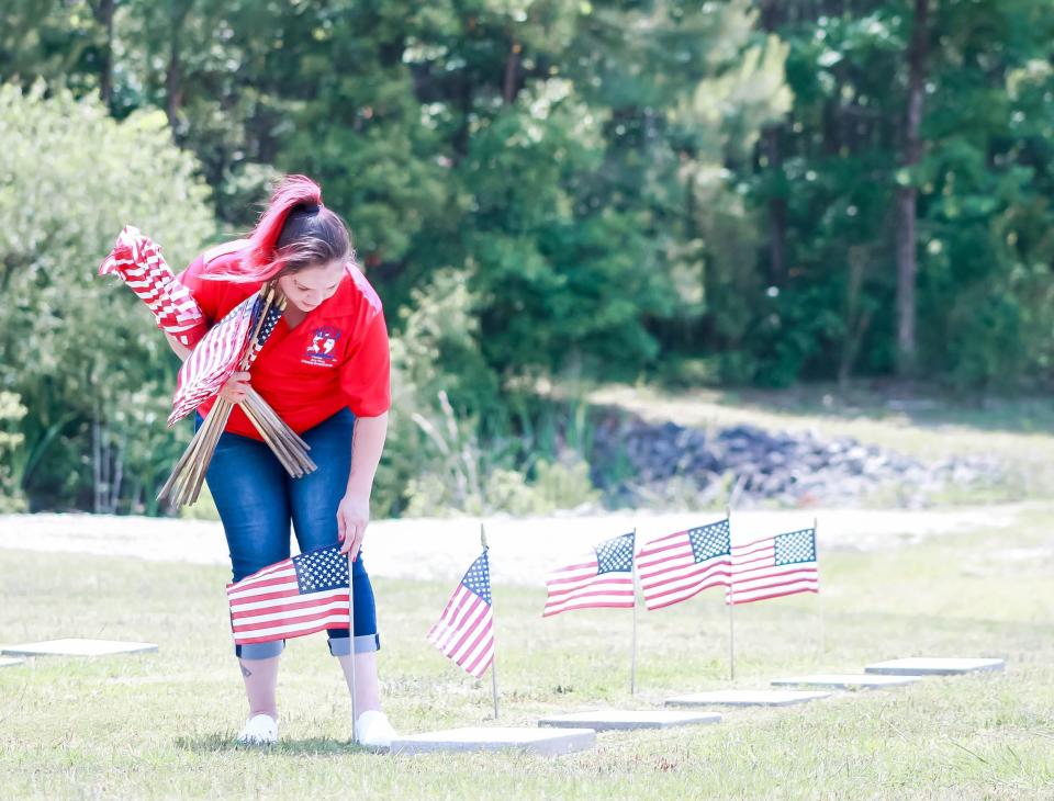 Amy Perez, Jacksonville community development director with Remember Everyone Deployed (R.E.D.), places American flags at the Coastal Carolina State Veterans Cemetery in Jacksonville in honor of Memorial Day on Friday, May 28, 2021.