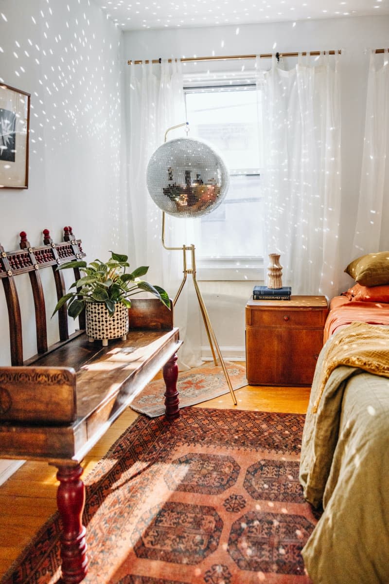 A disco ball hangs from stand in white bedroom with rust accents.