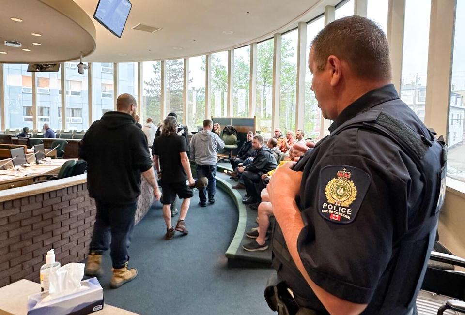 A Cape Breton regional police officer watches as tow truck operators file into the council chambers for second reading of the bylaw at Tuesday's meeting.