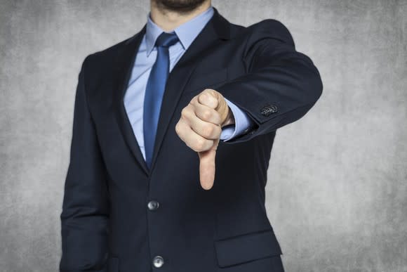 A businessman in a suit giving the thumbs-down sign.