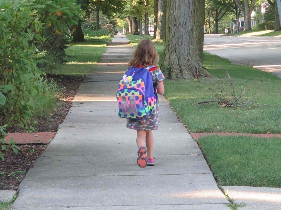 Girl walking to school with backpack on sidewalk