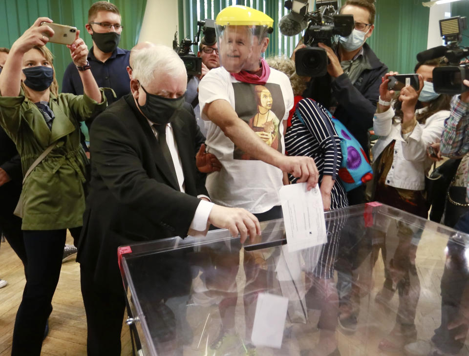 Leader of Poland's right-wing ruling party Jaroslaw Kaczynski, left, wearing a face mask for protection against the coronavirus, casts his ballot in the presidential election runoff in Warsaw, Poland, on Sunday, July 12, 2020, next to a man wearing a face mask of Kaczynski's likeness. The ruling Law and Justice party is backing the reelection bid of incumbent conservative President Andrzej Duda, against the liberal Warsaw Mayor Rafal Trzaskowski. Latest opinion polls suggested that the runoff will be decided by a very narrow margin. (AP Photo)