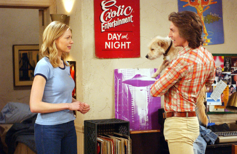A woman talks to a man holding a dog with the sign "Exotic entertainment day and night" on the wall between them